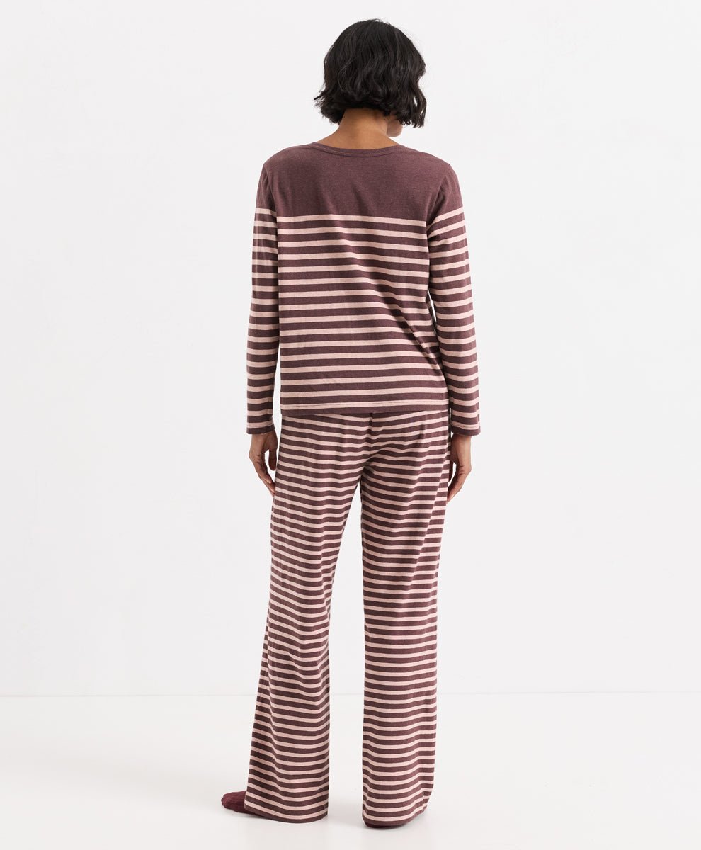 A model viewed from the back wearing a matching two-piece loungewear set consisting of a long-sleeve top and wide-leg pants, both featuring a horizontal stripe pattern in merlot and clay.