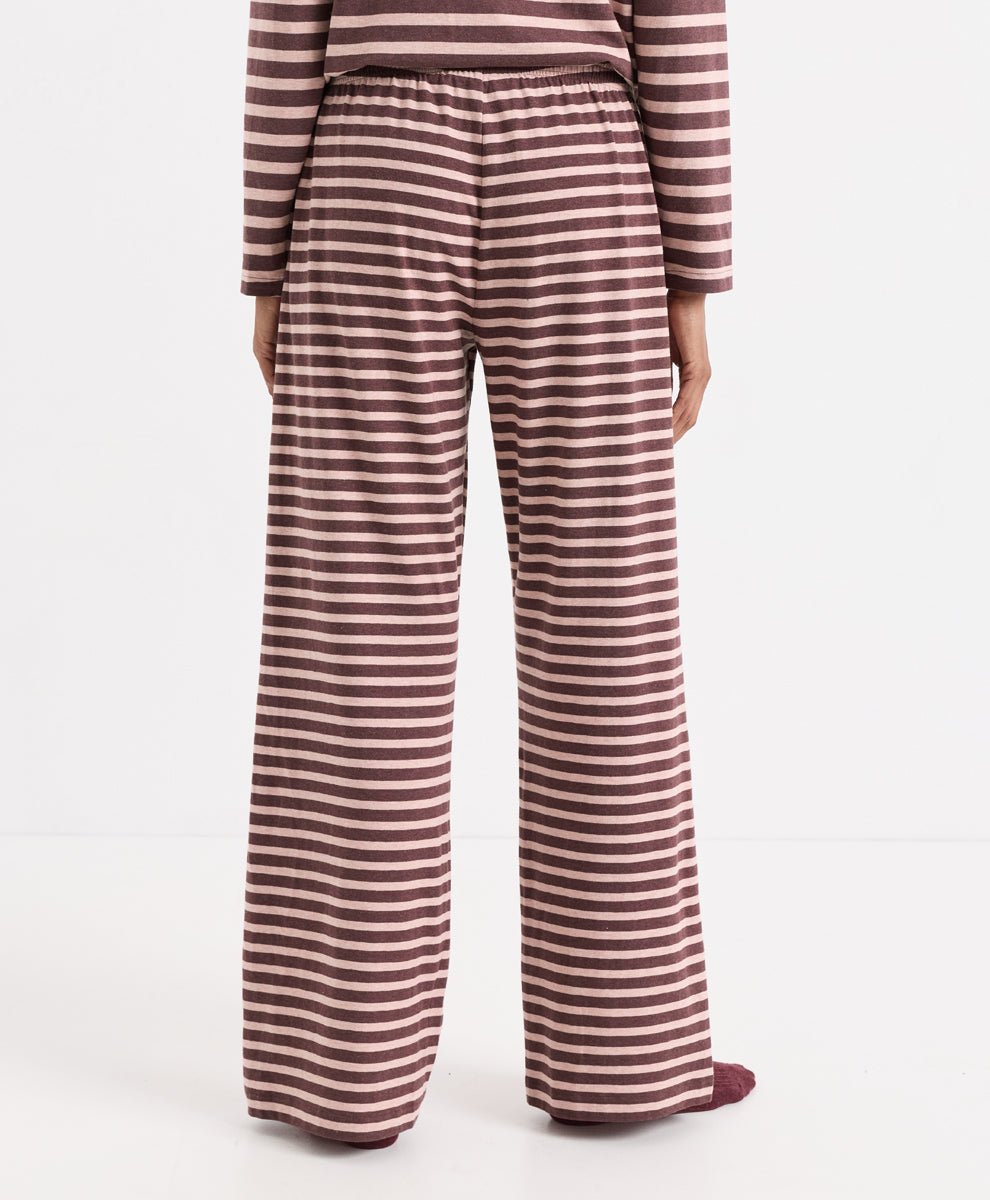 A person shown from the back wearing wide-leg pajama pants with horizontal merlot and clay stripes, paired with a matching striped long-sleeve top, against a plain white studio background.
