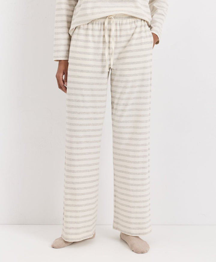 A person wearing loose, wide-leg pajama pants with thin horizontal beige and off-white stripes, paired with a matching long-sleeve top and socks, photographed against a plain light background.