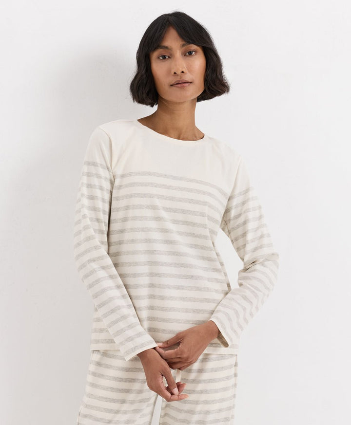 A woman wearing a long-sleeve striped top and matching pants in a cream and light gray colorway, standing against a plain white studio background.