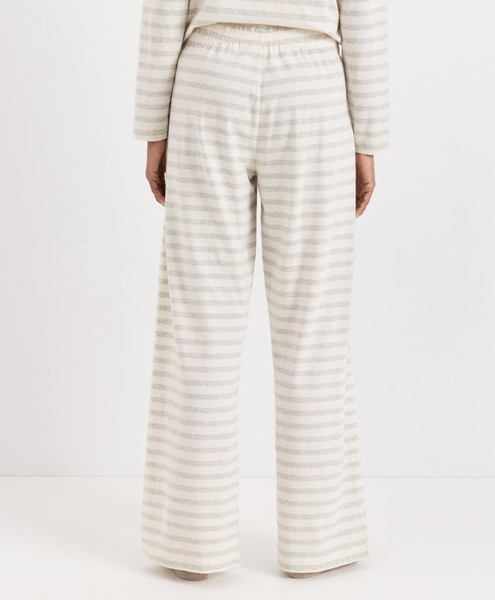 A person shown from the back wearing a matching striped lounge set, featuring wide-leg pants and a long-sleeve top in a cream and light beige stripe pattern, against a plain white studio background.