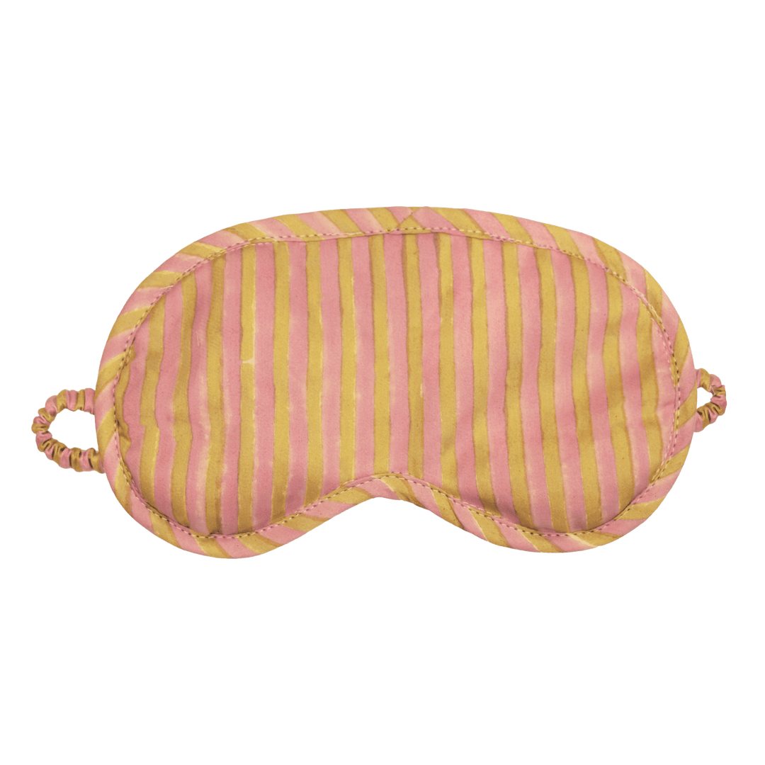 A striped sleep mask with alternating vertical pink and mustard yellow stripes, featuring a padded eye area, stitched edges, and elastic ear loops on a plain white background.