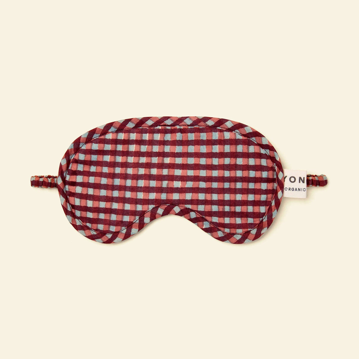 A red and white gingham patterned sleep mask with adjustable ear loops and a small white brand tag reading 'Yonder' on a light cream background.