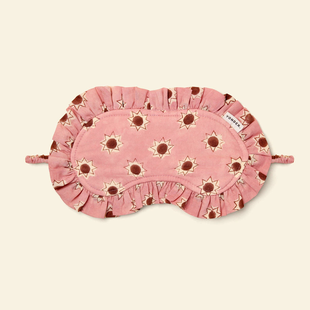 Yonder pink sleep mask with a sunflower pattern, featuring ruffled edges, shown on a light cream background. 