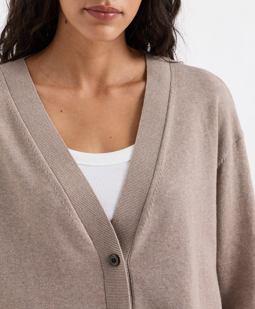 Close-up of a woman wearing a soft umber heather beige V-neck cardigan over a white ribbed tank top, against a clean white background.