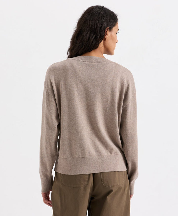 A woman shown from the back wearing a soft umber heather knit sweater and olive brown trousers against a plain white studio background.