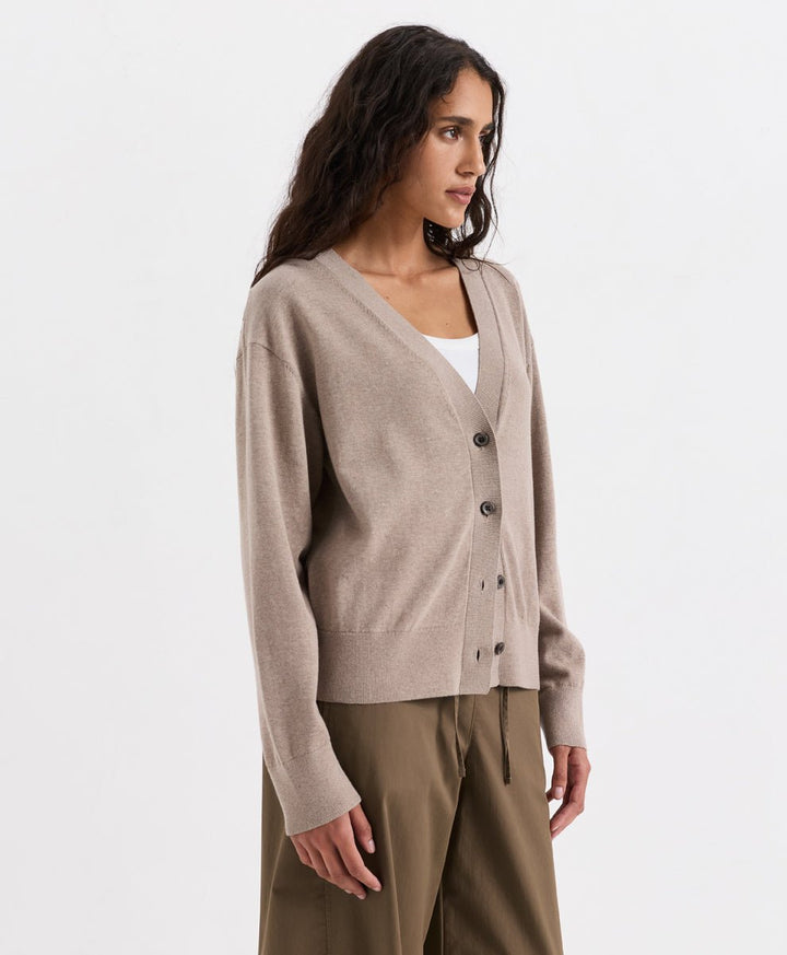 A woman wearing a soft umber heather knit cardigan over a white top and olive green trousers, photographed against a clean white studio background.