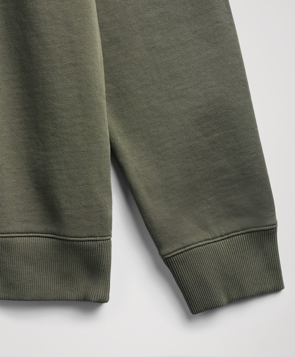 Close-up of a dusted green sweatshirt sleeve showing the ribbed cuff and textured fabric against a light gray background.