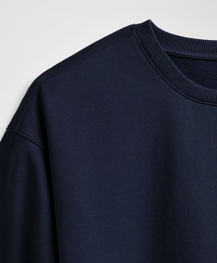 Close-up of a dark navy crewneck sweatshirt showing the ribbed collar and shoulder seam against a light gray background.
