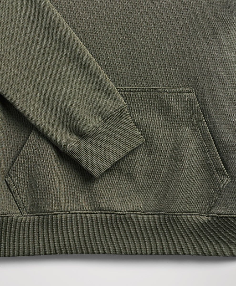 Close-up of a dusted green sweatshirt showing the sleeve cuff, ribbed hem, and a front kangaroo pocket.