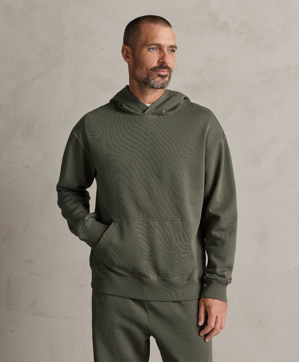 A man wearing a pact dusted green textured hoodie and matching sweatpants, standing against a neutral textured gray wall.
