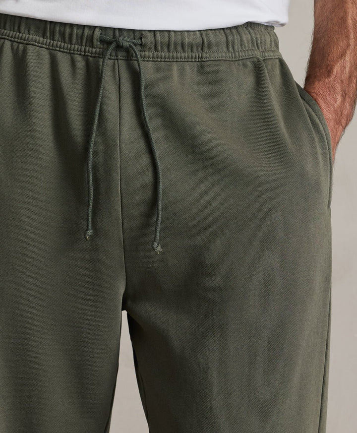 Close-up of a person wearing dusted green drawstring sweatpants with a white shirt partially visible at the top, against a plain light background.