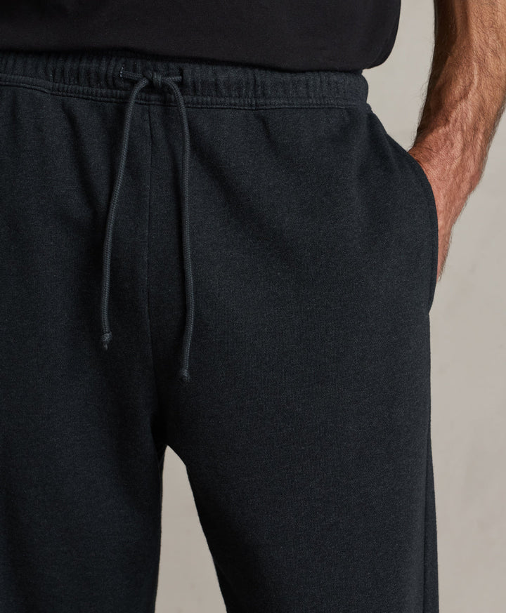 Close-up of a person wearing charcoal heather sweatpants with an elastic drawstring waistband and side pocket, paired with a black top against a light neutral background.
