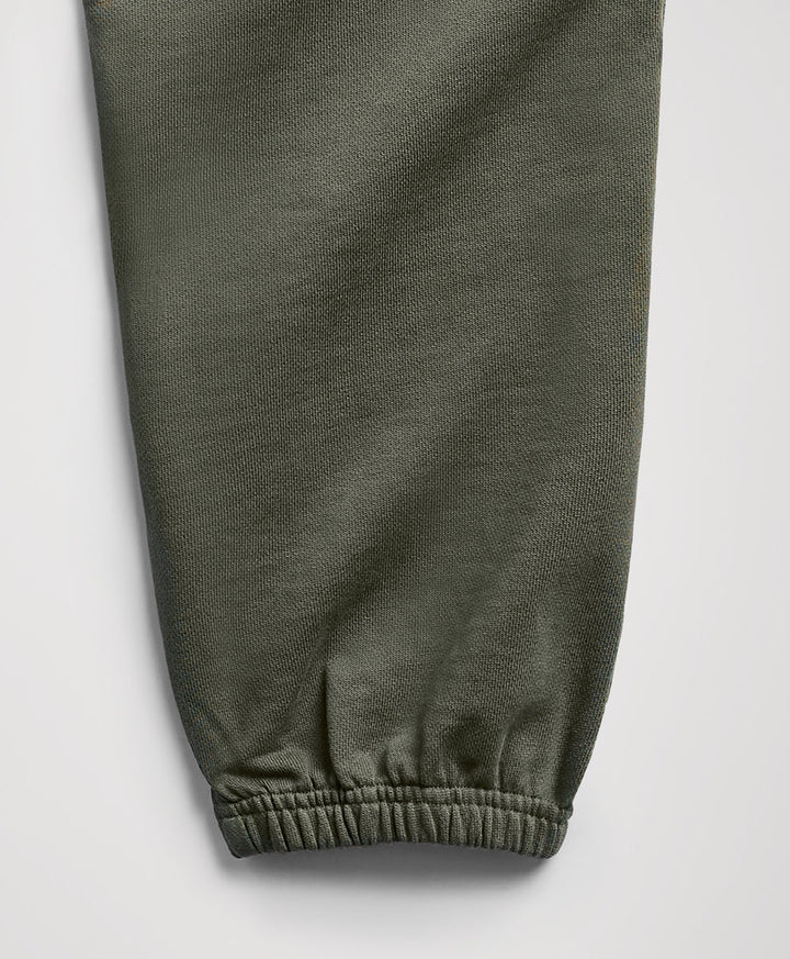 Close-up of an dusted green fabric pant leg with an elasticized cuff, shown against a light gray background.