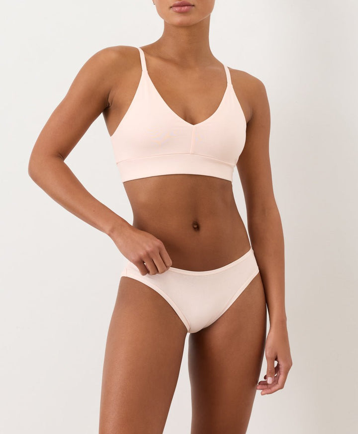 Woman wearing a light pink bikini set on a plain background