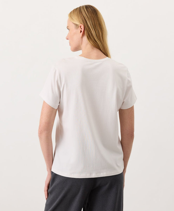 Woman wearing a Pact cream Organic Luxe Essential Crewneck Tee
 and dark pants against a plain background