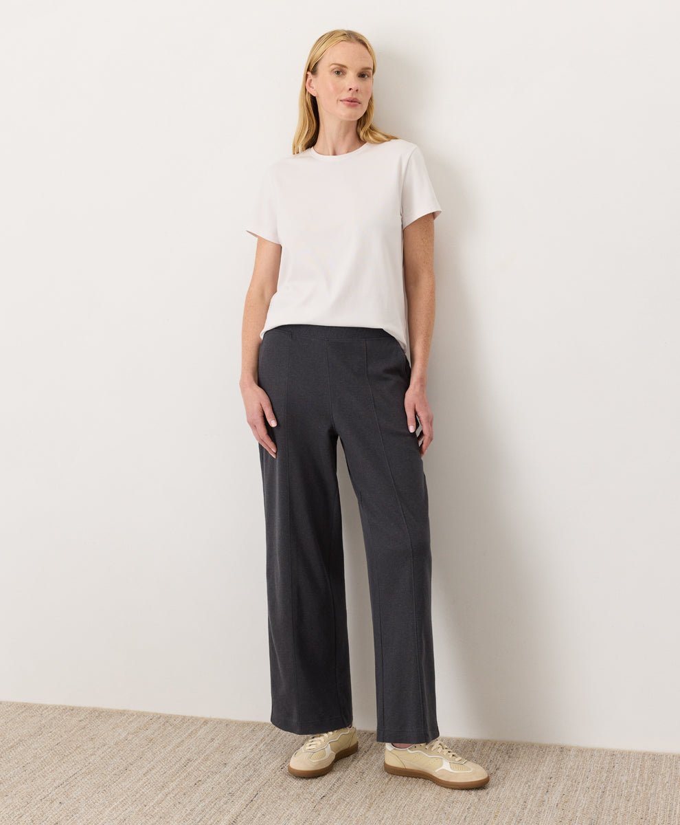 Woman wearing a Pact cream Organic Luxe Essential Crewneck Tee
 and dark pants against a plain background