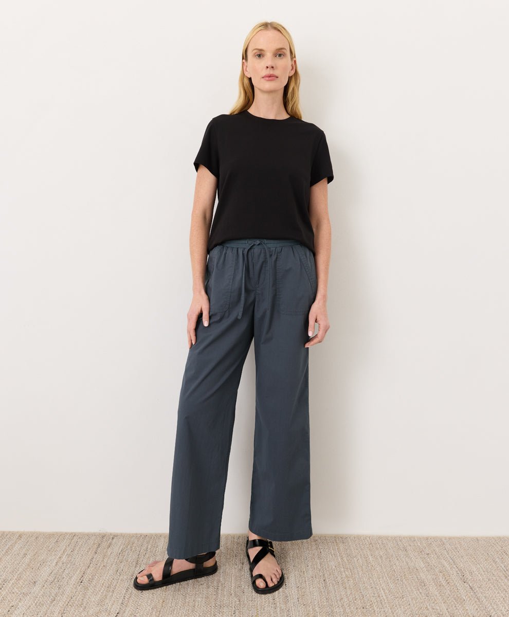 Woman wearing a Pact black Organic Luxe Essential Crewneck Tee
 and dark pants against a plain background