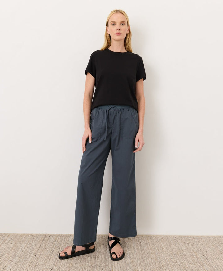 Woman wearing a Pact black Organic Luxe Essential Crewneck Tee
 and dark pants against a plain background