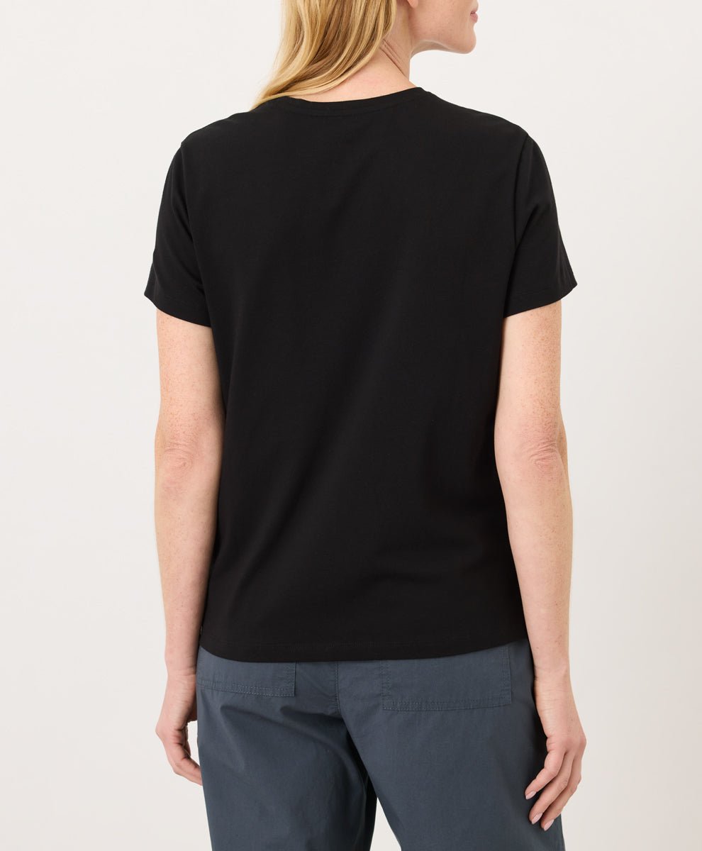 Woman wearing a Pact black Organic Luxe Essential Crewneck Tee
 and dark pants against a plain background