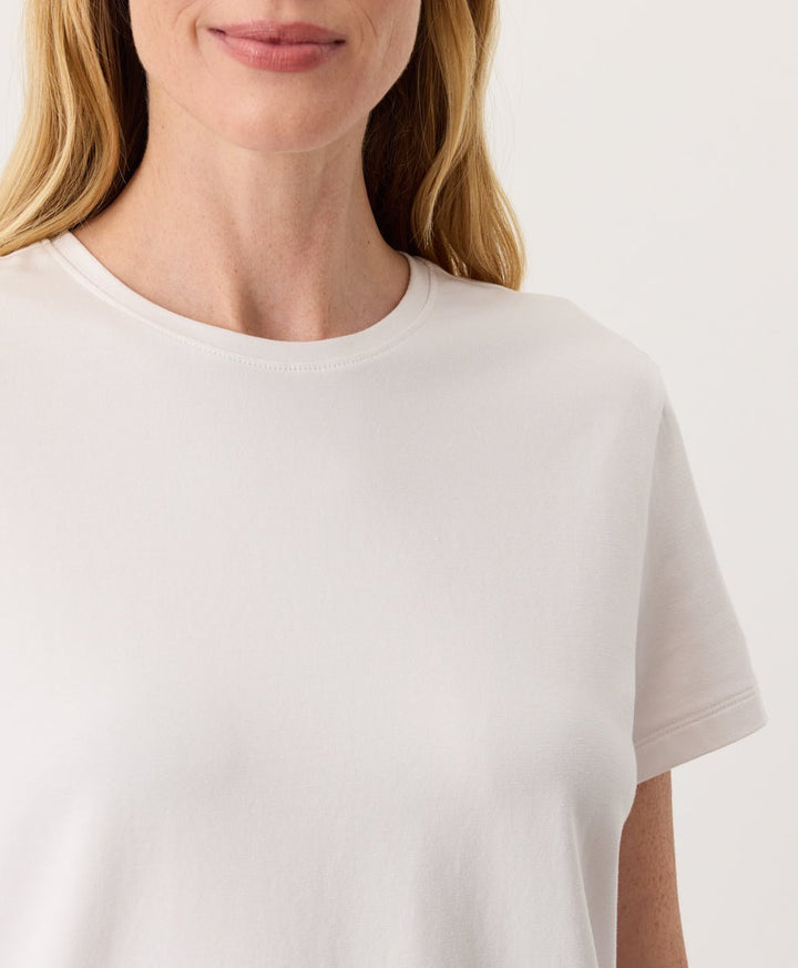 Woman wearing a Pact cream Organic Luxe Essential Crewneck Tee against a plain background