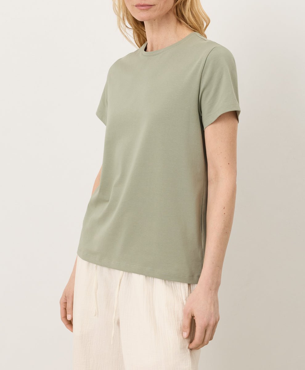 Woman wearing a Pact seagrass Organic Luxe Essential Crewneck Tee and cream pants against a plain background