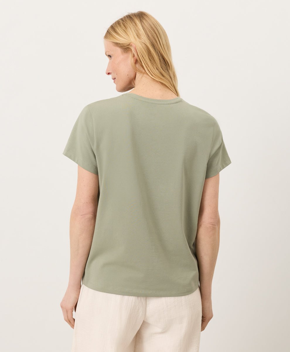 Woman wearing a Pact seagrass Organic Luxe Essential Crewneck Tee and cream pants against a plain background