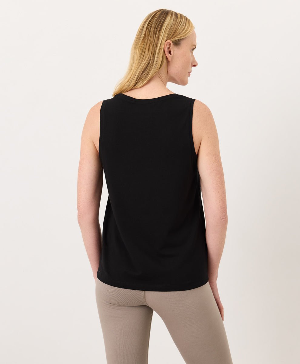 Woman wearing a black Pact Organic Luxe Essential Scoop Neck Tank and cinder leggings against a white background