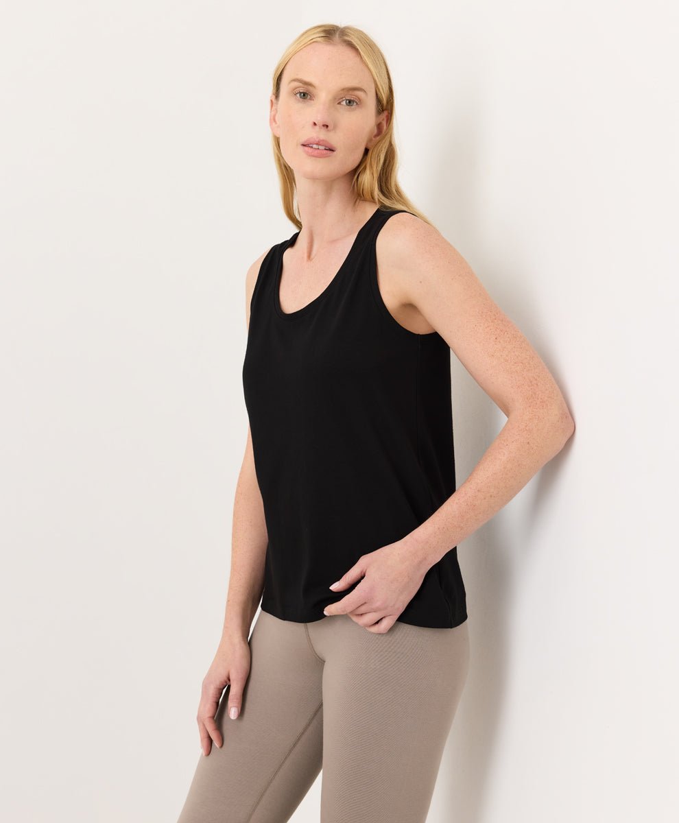 Woman wearing a black Pact Organic Luxe Essential Scoop Neck Tank and cinder leggings against a white background