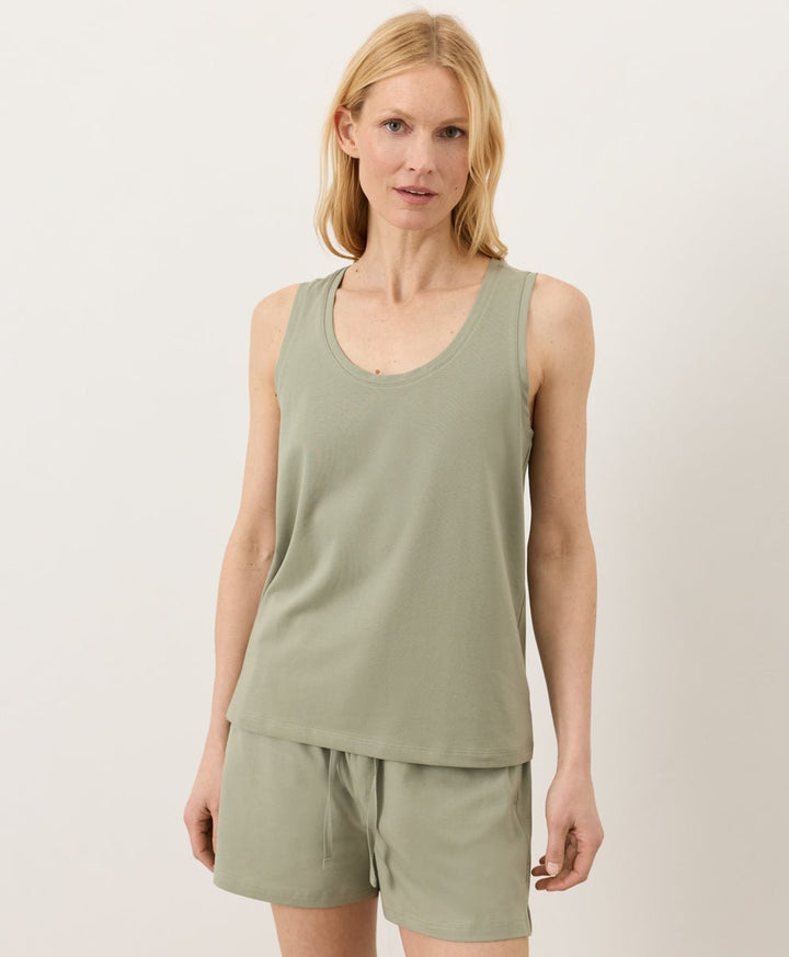 Woman wearing a seagrass Pact Organic Luxe Essential Scoop Neck Tank and seagrass shorts against a white background