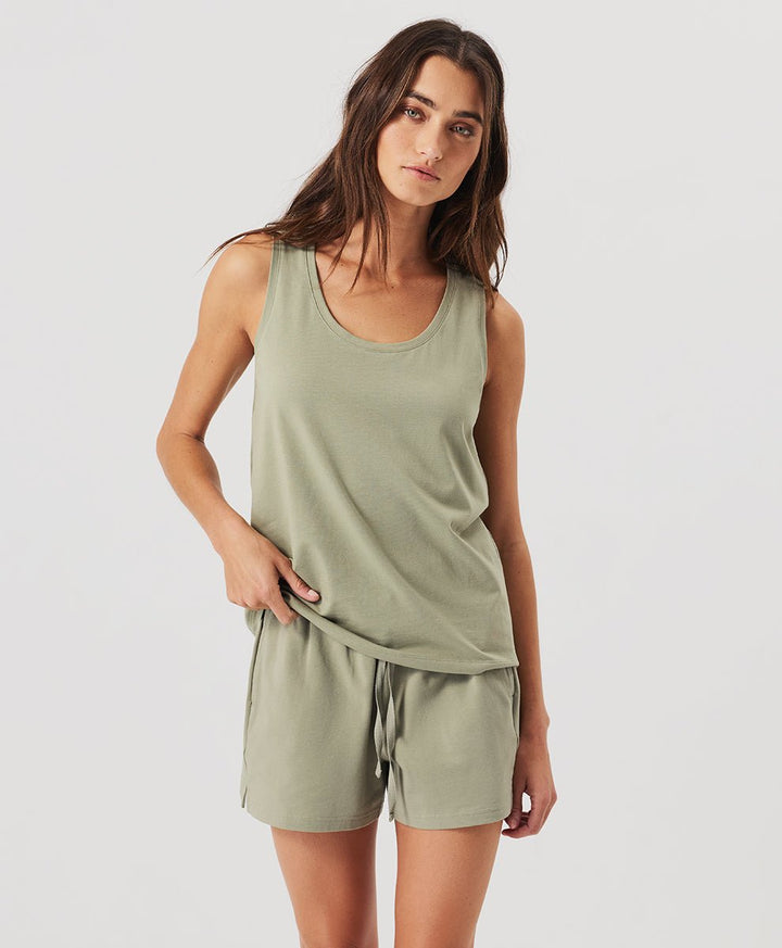 Woman wearing a seagrass Pact Organic Luxe Essential Scoop Neck Tank and seagrass shorts against a white background