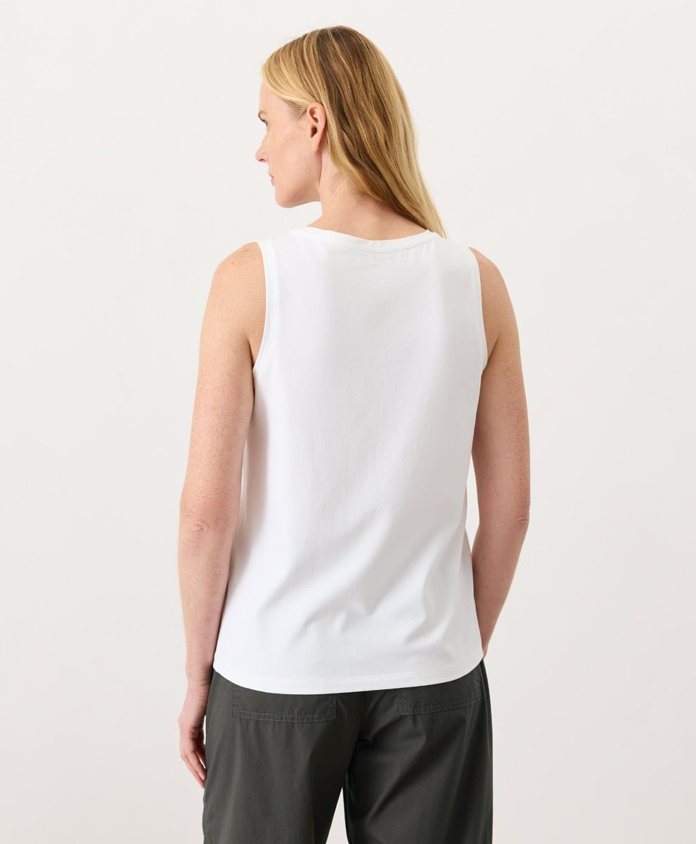 Woman wearing a white Pact Organic Luxe Essential Scoop Neck Tank and dark pants against a white background