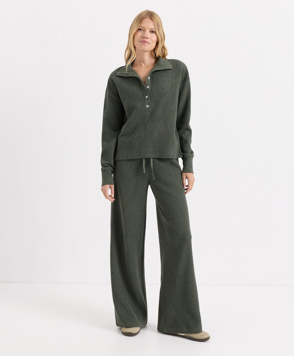 A woman modeling a matching dusted green heather loungewear set consisting of a long-sleeve half-placket henley top and wide-leg drawstring pants, photographed against a clean white studio background.