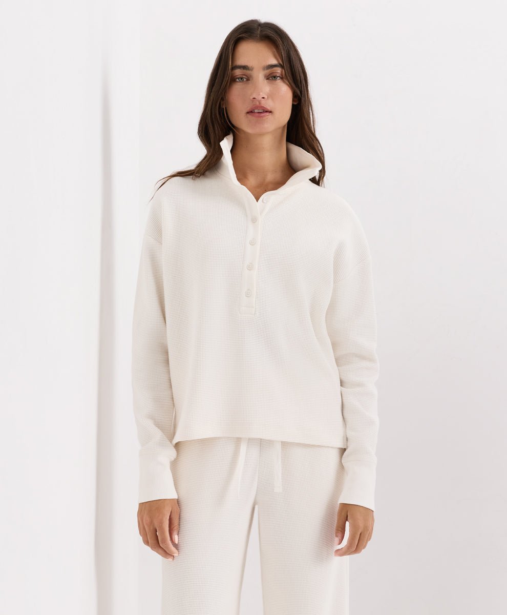 A woman modeling a soft ivory knit long-sleeve henley top with matching pants against a clean white studio background.
