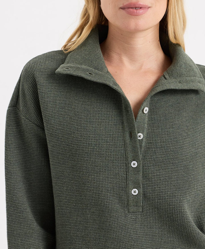 Close-up of a woman wearing a dusted green heather waffle-knit long-sleeve henley with white buttons.