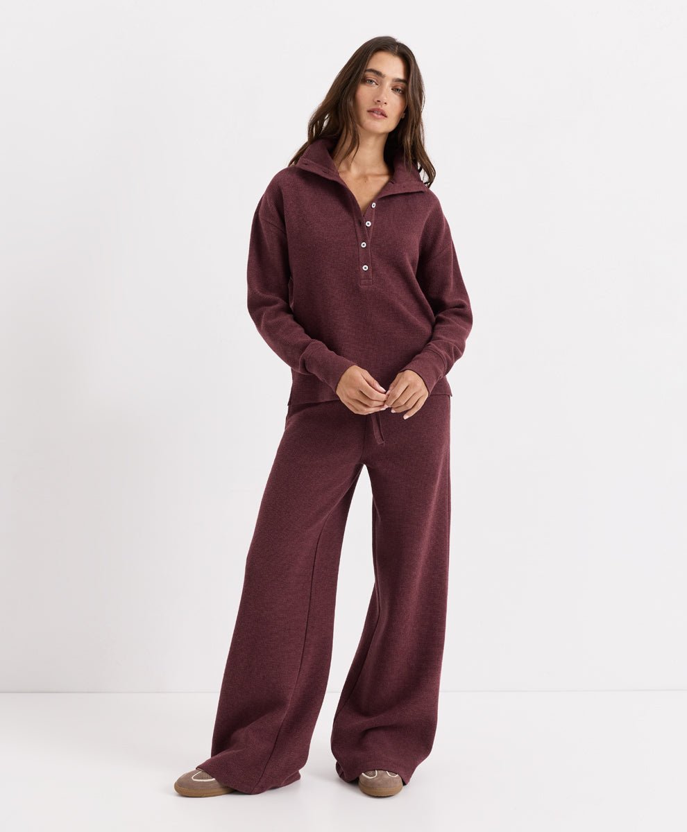 A woman modeling a matching two-piece loungewear set in merlot heather, featuring a long-sleeve half-button henley top and wide-leg pants, against a plain white studio background.