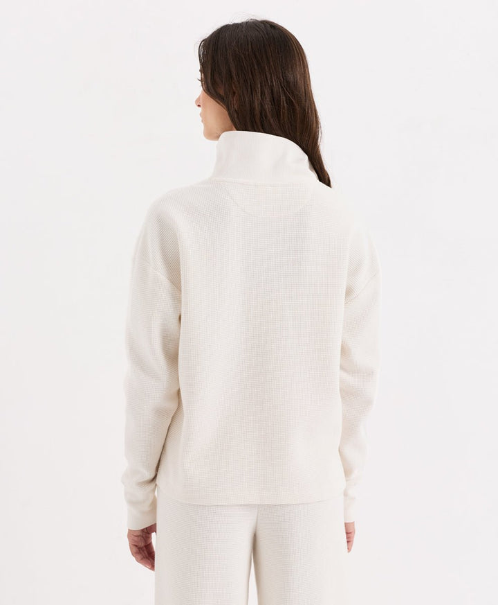 A woman shown from the back wearing a soft ivory henley with matching pants, against a plain white studio background.