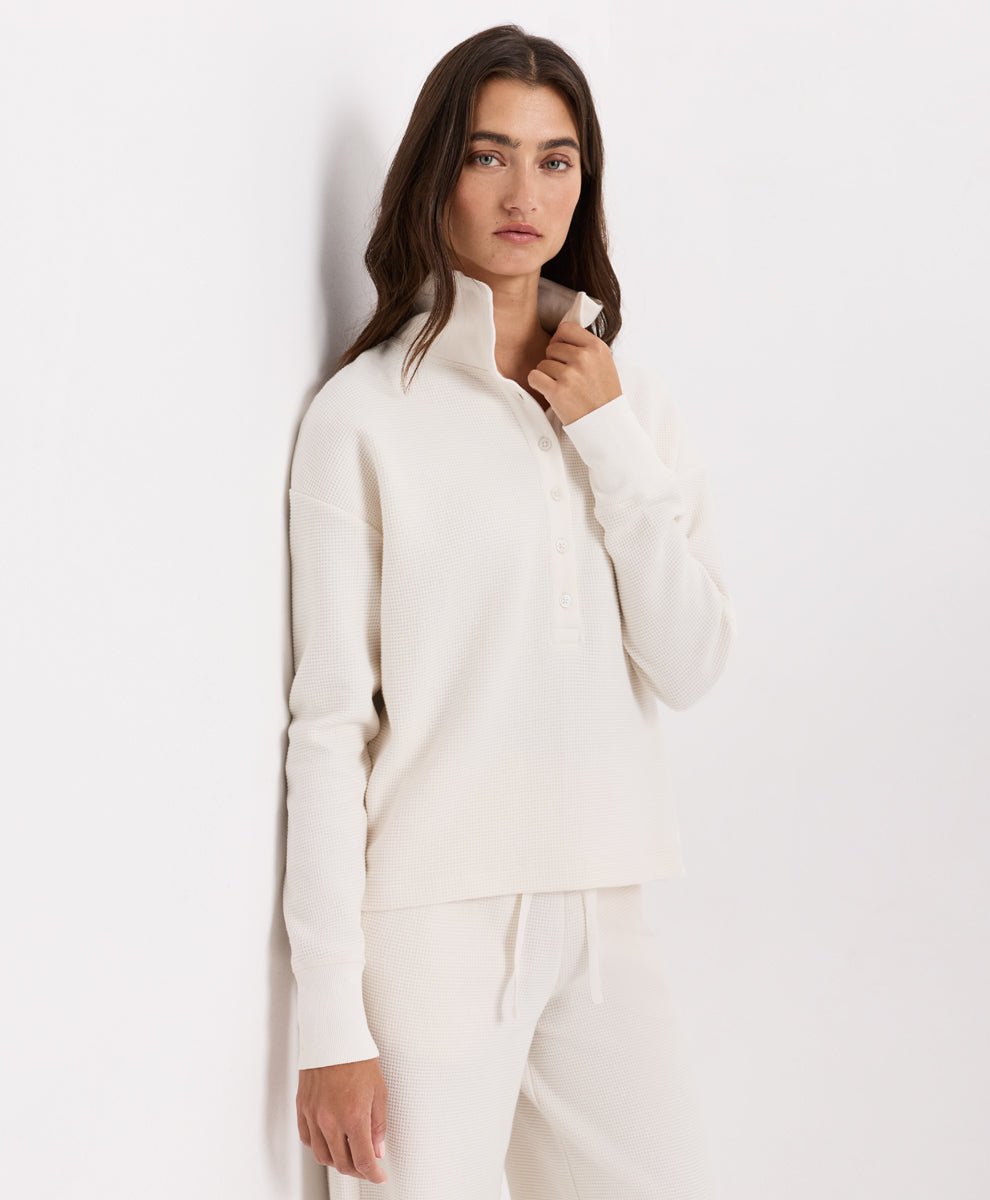A woman modeling a soft ivory knit henley with matching drawstring pants against a plain white studio background.