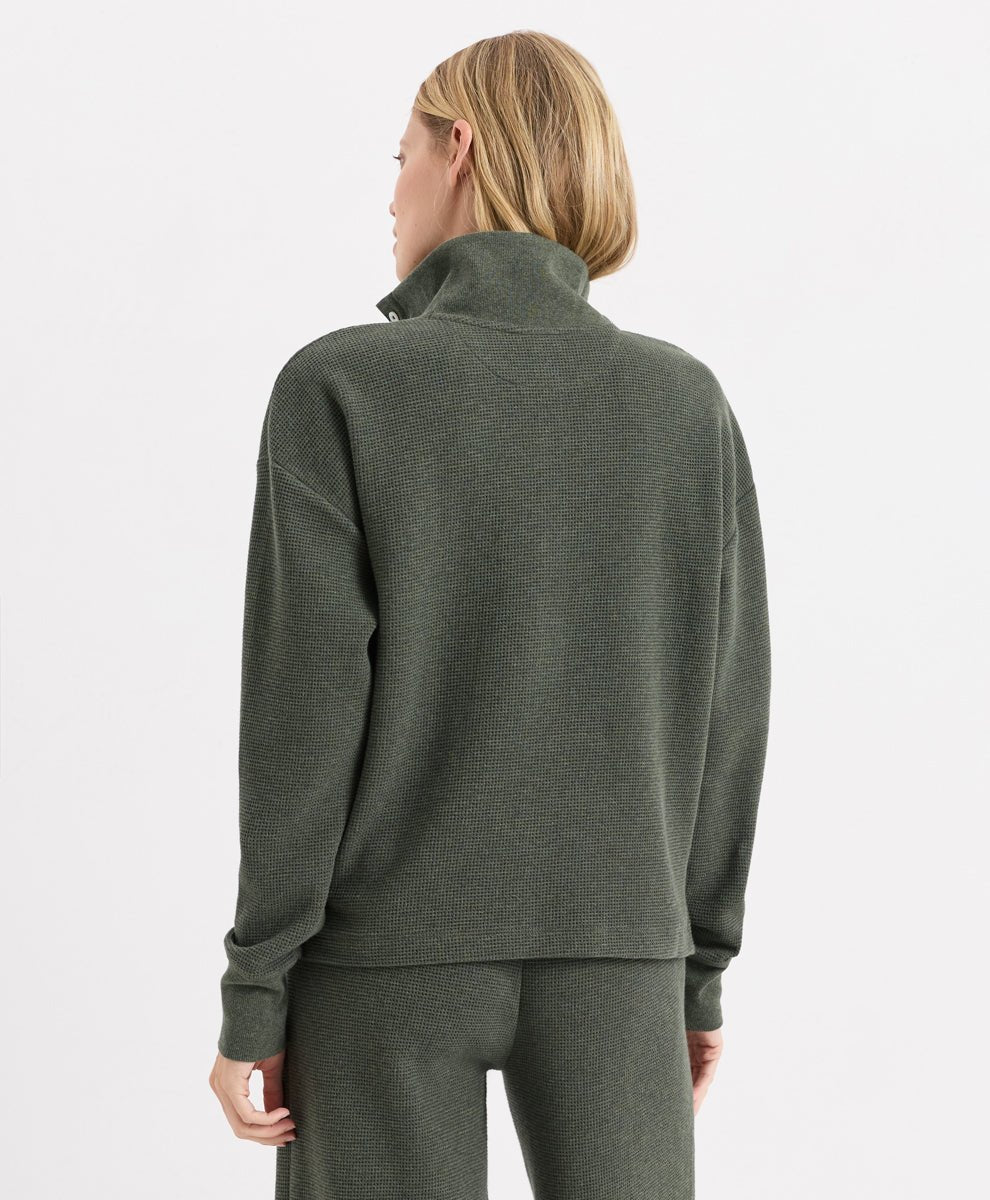 A woman shown from the back wearing an dusted green heather henley and matching sweatpants against a light gray studio background.