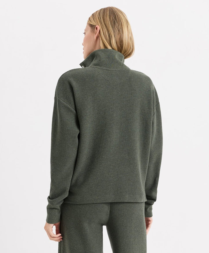 A woman shown from the back wearing an dusted green heather henley and matching sweatpants against a light gray studio background.