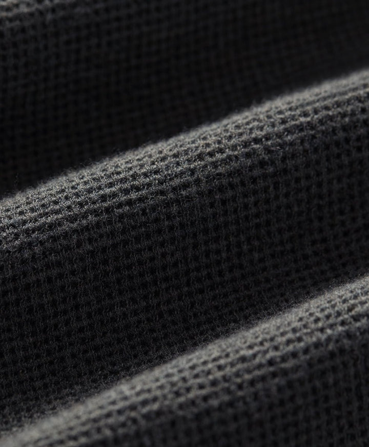 Close-up of a dark charcoal heather waffle-knit fabric texture with soft diagonal folds.