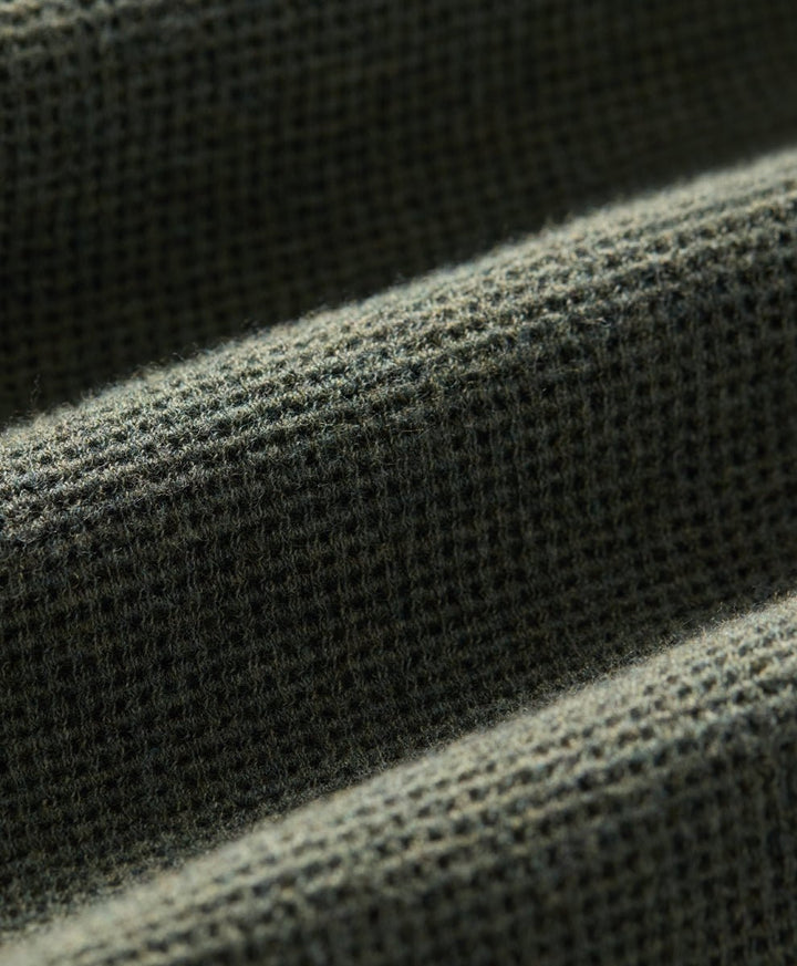 Close-up of a dusted green heather waffle-knit fabric texture with soft diagonal folds.