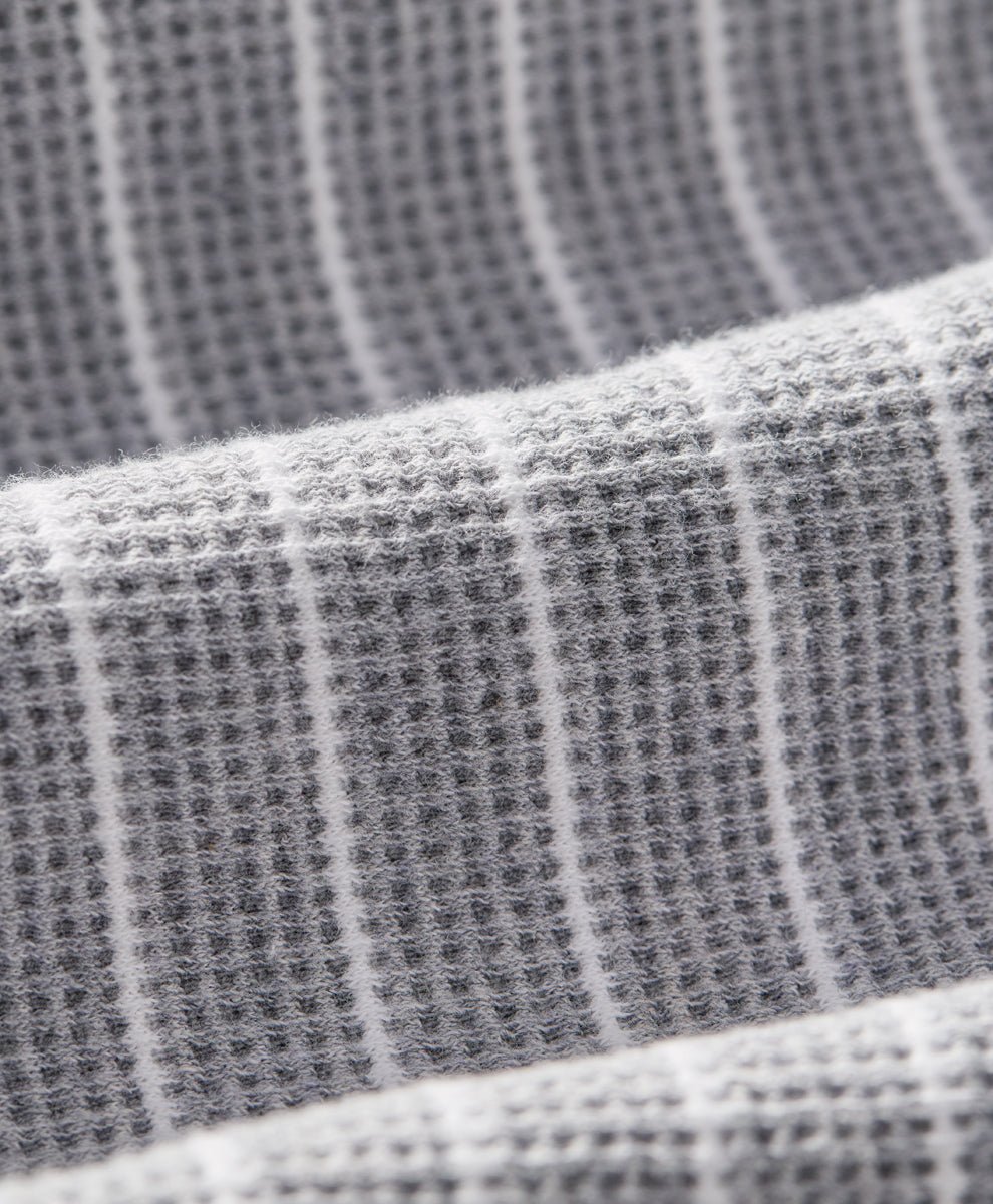 Close-up of a gray waffle-weave fabric with thin white vertical stripes, showing the textured weave and soft folds.