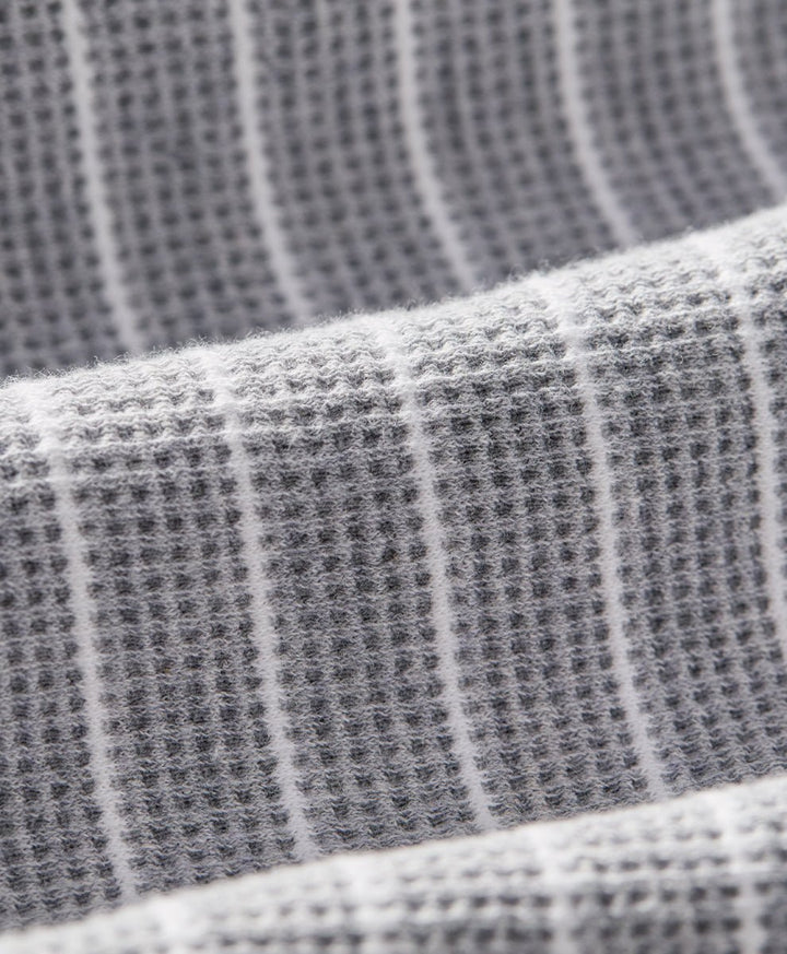 Close-up of a gray waffle-weave fabric with thin white vertical stripes, showing the textured weave and soft folds.