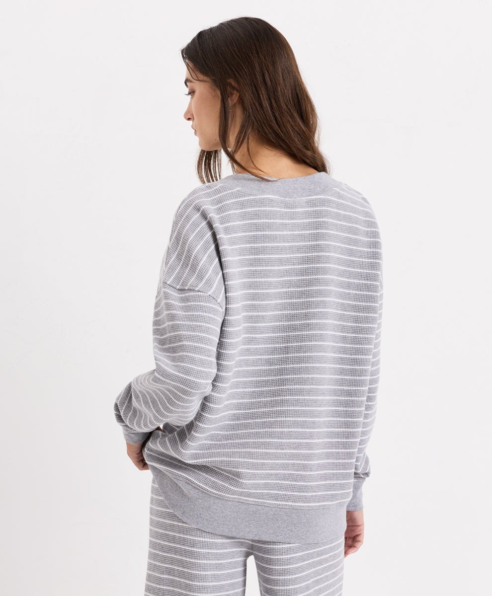 A woman shown from the back wearing a light gray and white horizontally striped V-neck top and matching striped pants against a plain white studio background.