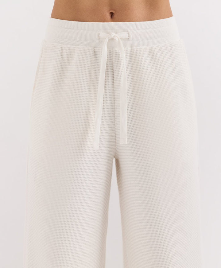 Close-up of a person wearing textured soft ivory wide-leg lounge pants with a matching drawstring waistband, shown against a plain light background.