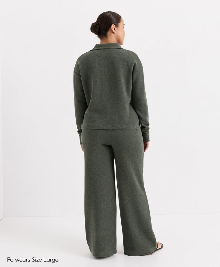A woman shown from the back wearing a matching dusted green heatherknit lounge set consisting of a long-sleeve Henley top and wide-leg pants, photographed against a clean white studio background.