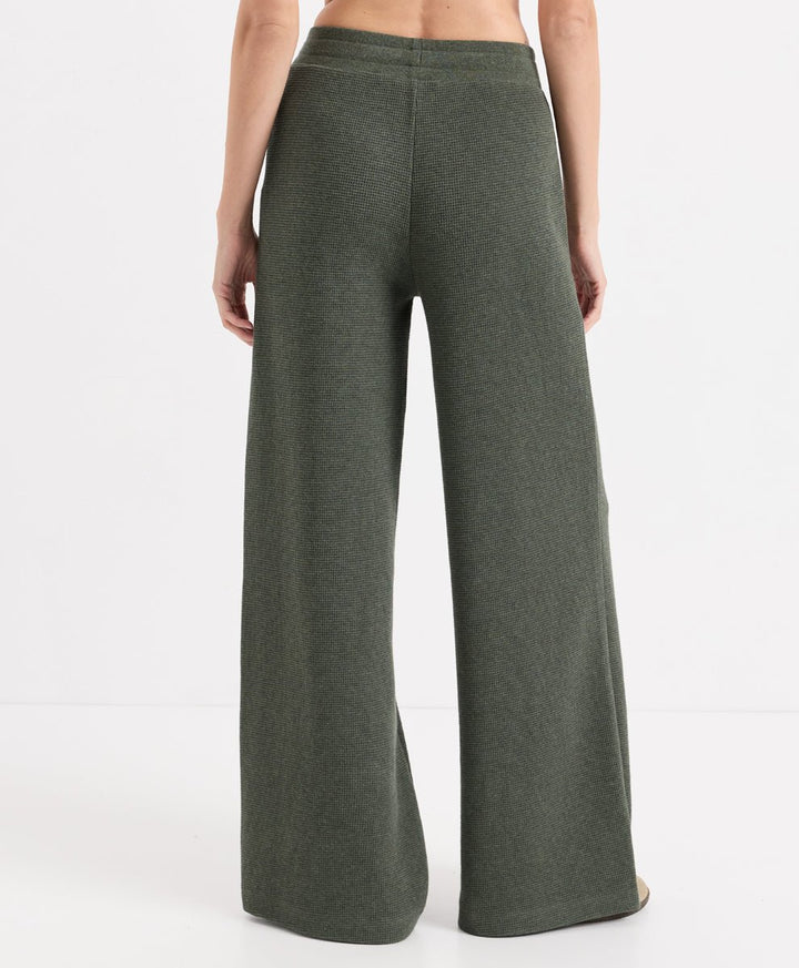 A model shown from the back wearing dusted green heather wide-leg knit pants against a clean white studio background.
