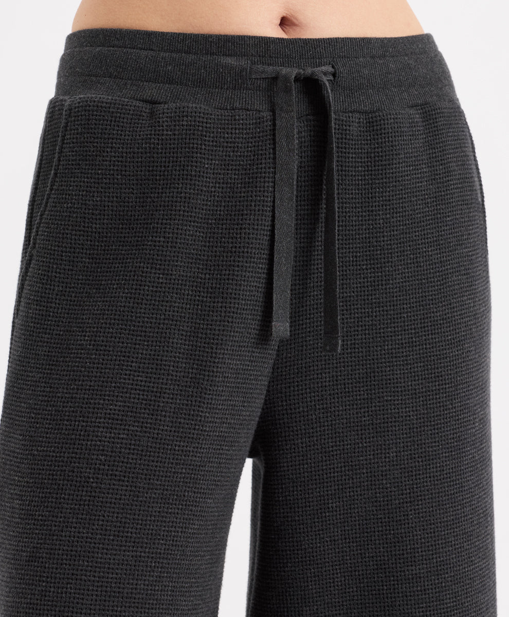 Close-up of a person wearing dark charcoal heather textured lounge pants with a matching drawstring waistband, shown against a light gray studio background.