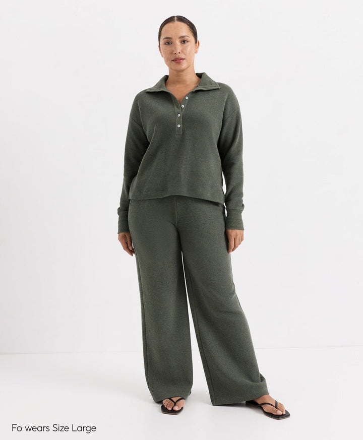 A woman modeling a matching two-piece lounge set in dusted green heather, featuring a long-sleeve henley top with a button placket and wide-leg pants, photographed against a plain white studio background.
